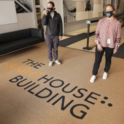 Two volunteers wearing LightHouse masks stand in the lobby of LightHouse headquarters. One holds a walkie-talkie.