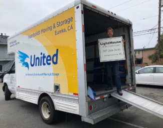 Janet Pomeranz standing in the opening of the Humboldt Moving and Storage Co. van holding a sign that says LightHouse of the North Coast