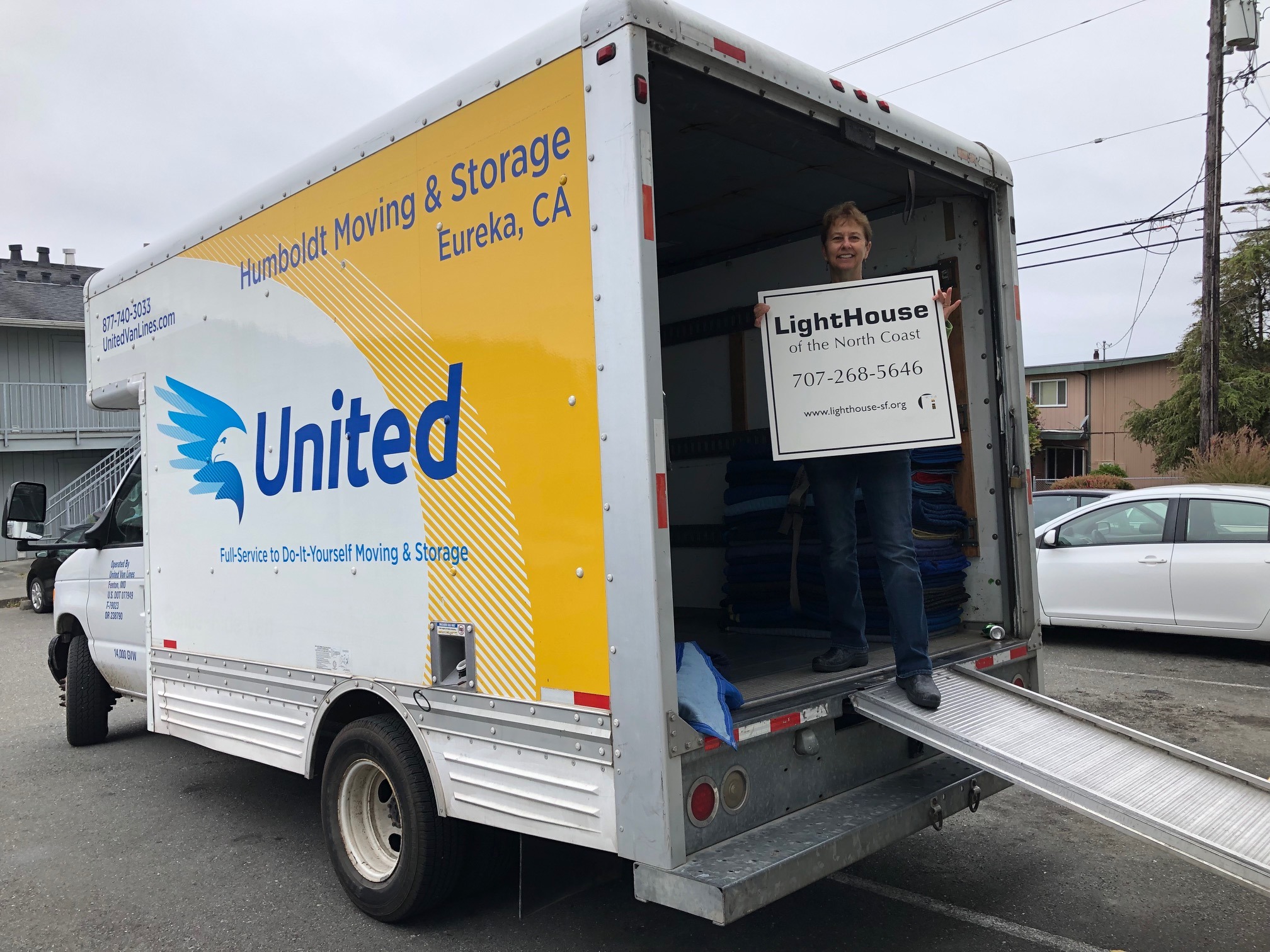 Janet Pomeranz standing in the opening of the Humboldt Moving and Storage Co. van holding a sign that says LightHouse of the North Coast