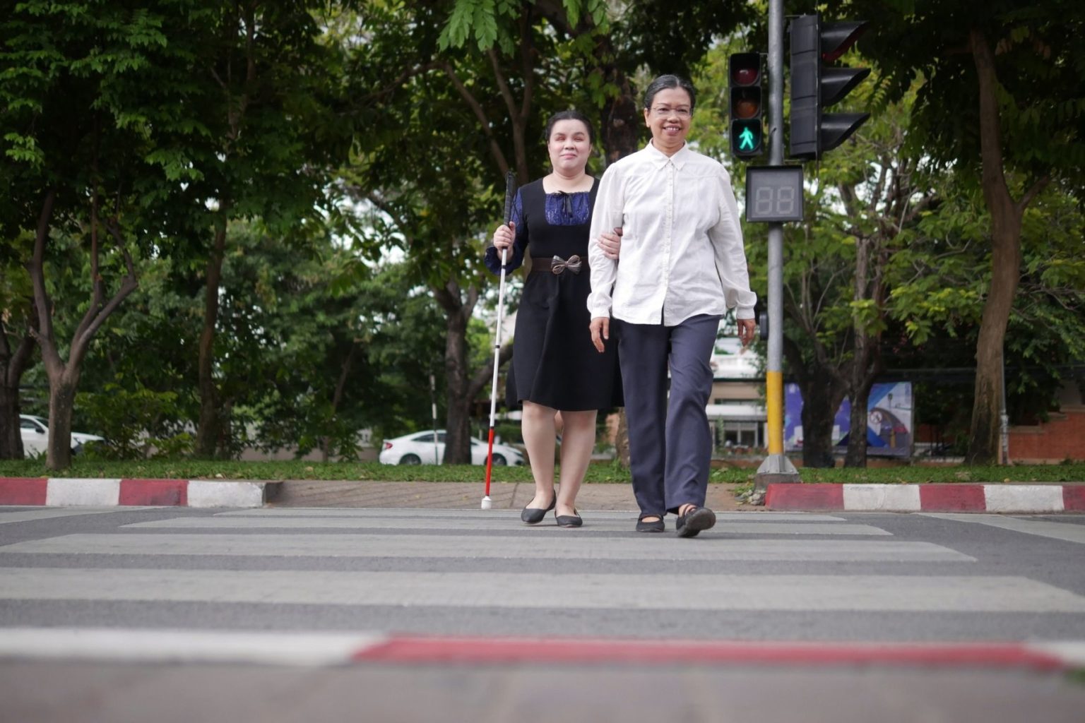 Two people cross an intersection with an APS. One is using a white cane