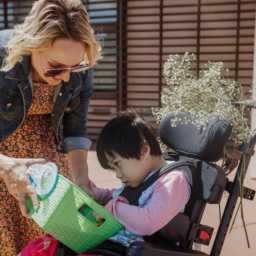 LightHouse Little Learners Specialist, Elizabeth, holds a sensory activity tray filled with beans and colorful plastic bugs for a little girl who is a wheelchair user