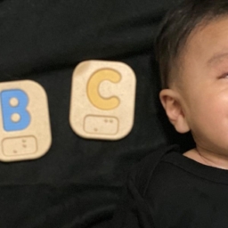 Little Learners ABC baby Little Learner is laying down next to ABC Braille blocks.