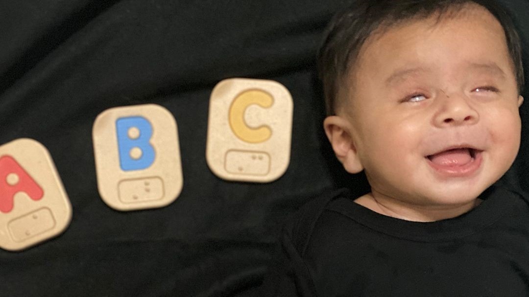 Little Learner is laying down next to ABC Braille blocks.