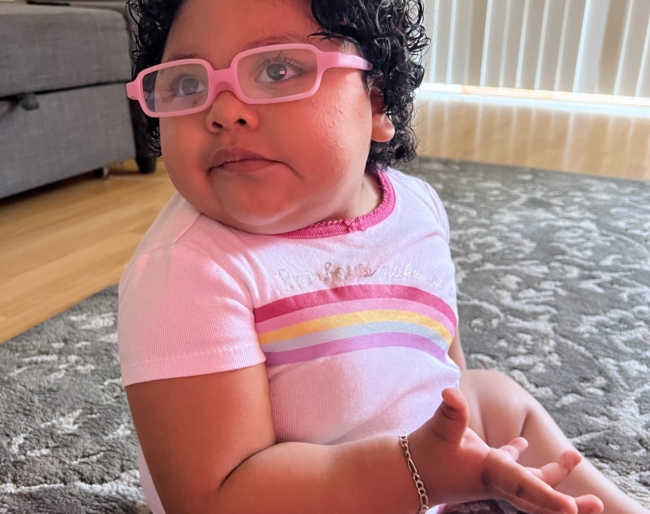 Little Learners girl wears glasses with a pink frame and a pink bow in her hair
