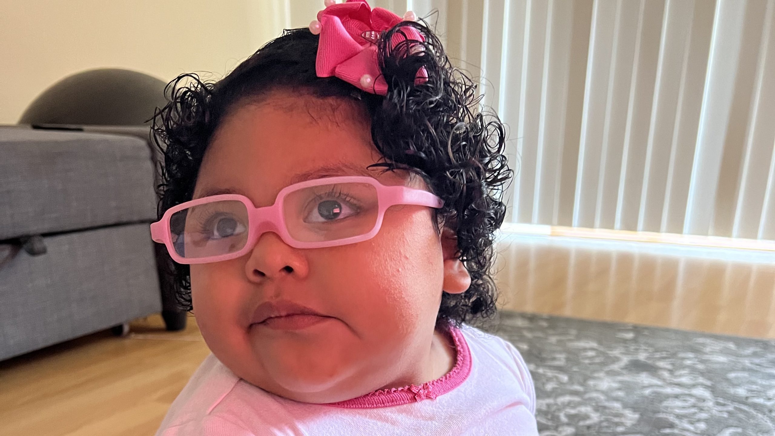 Little Learners girl wears glasses with a pink frame and a pink bow in her hair