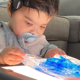 Little Learner with a pacifier in his mouth plays with a translucent blue material on a lightboard
