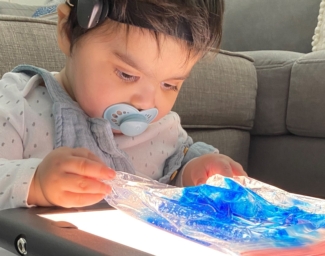 Little Learner with a pacifier in his mouth plays with a translucent blue material on a lightboard