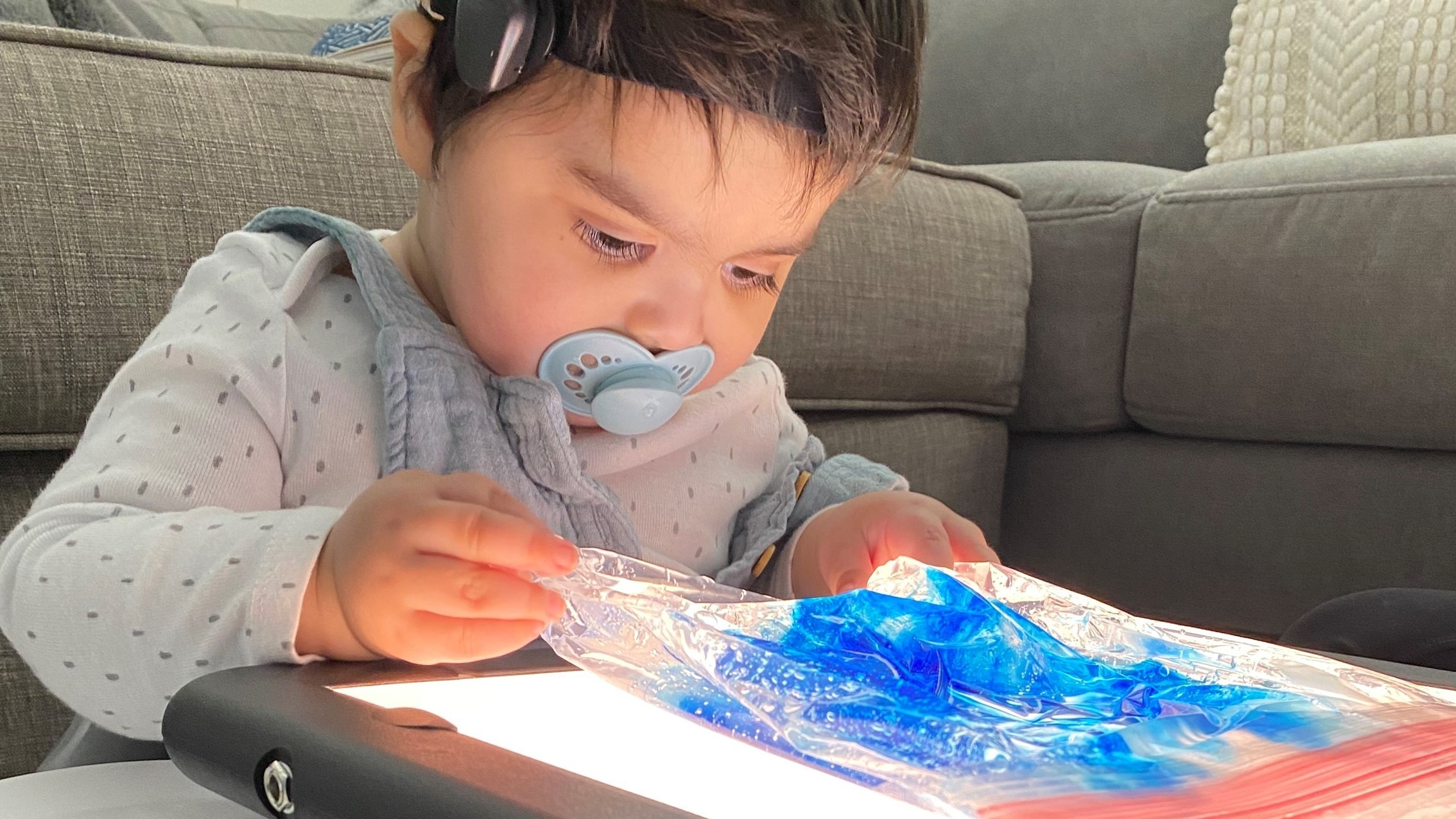 Little Learner with a pacifier in his mouth plays with a translucent blue material on a lightboard