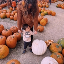 Little Learners Pumpkin A mother holds both of her son’s hands as they stand in a pumpkin patch