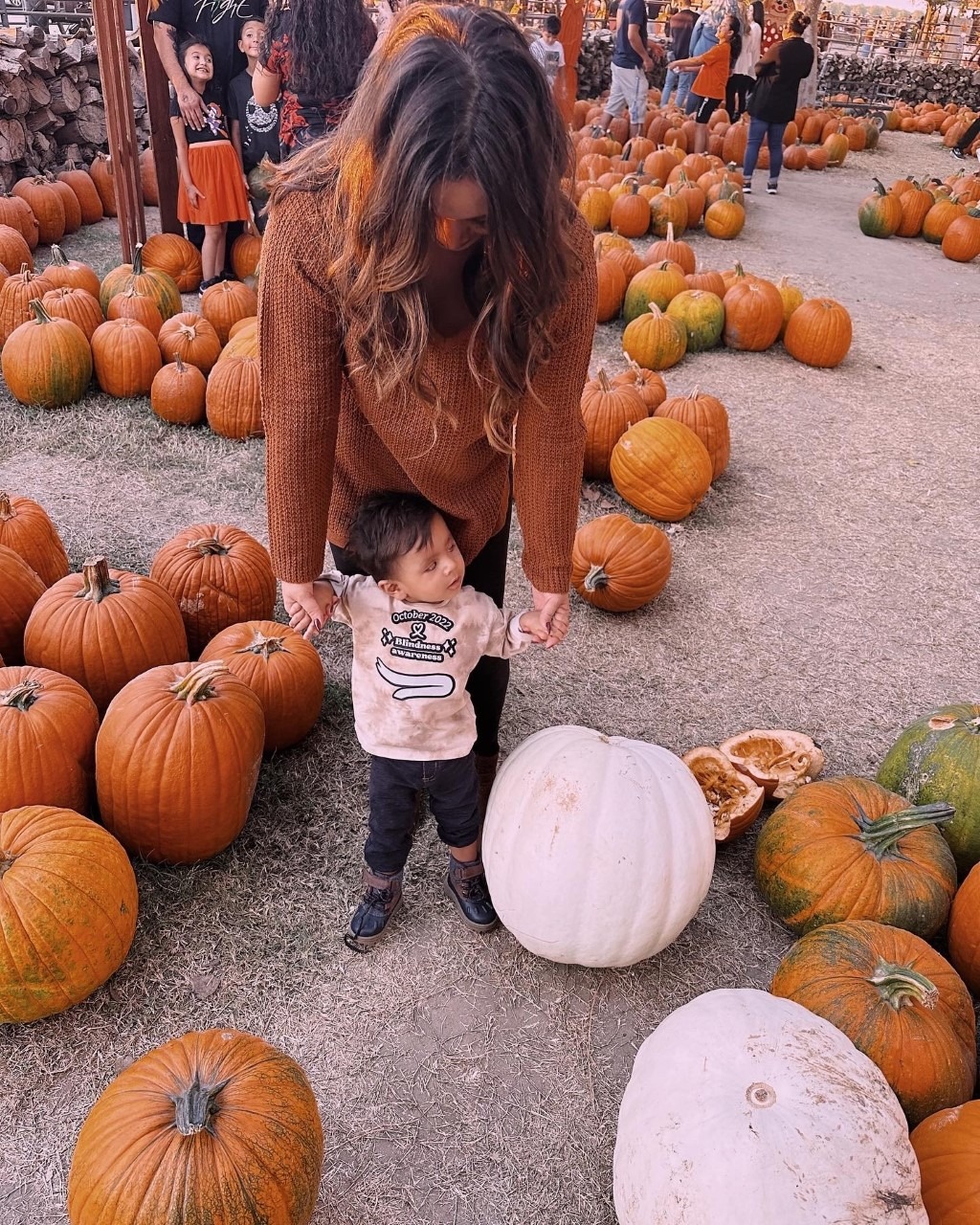 A mother holds both of her son’s hands as they stand in a pumpkin patch