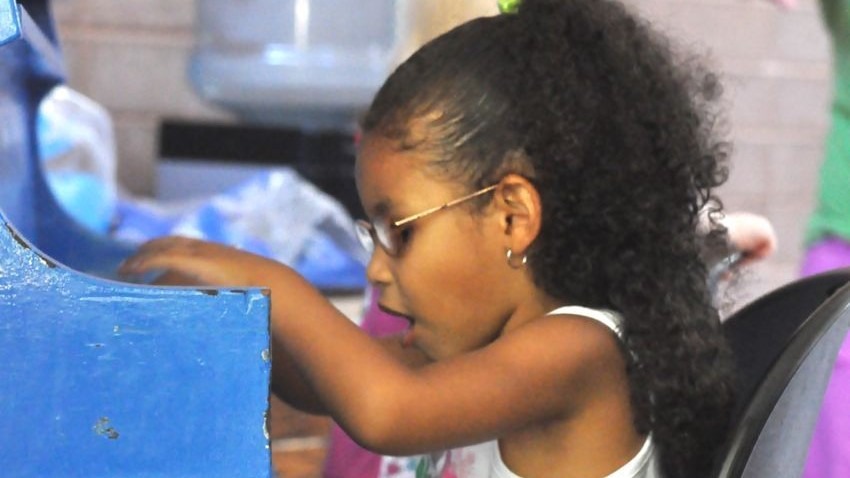 A little girl wearing glasses plays on a toy piano