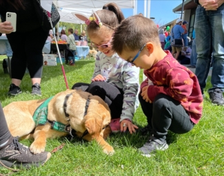 Two Little Learners kneel on the grass next to a yellow lab service dog who is off-harness