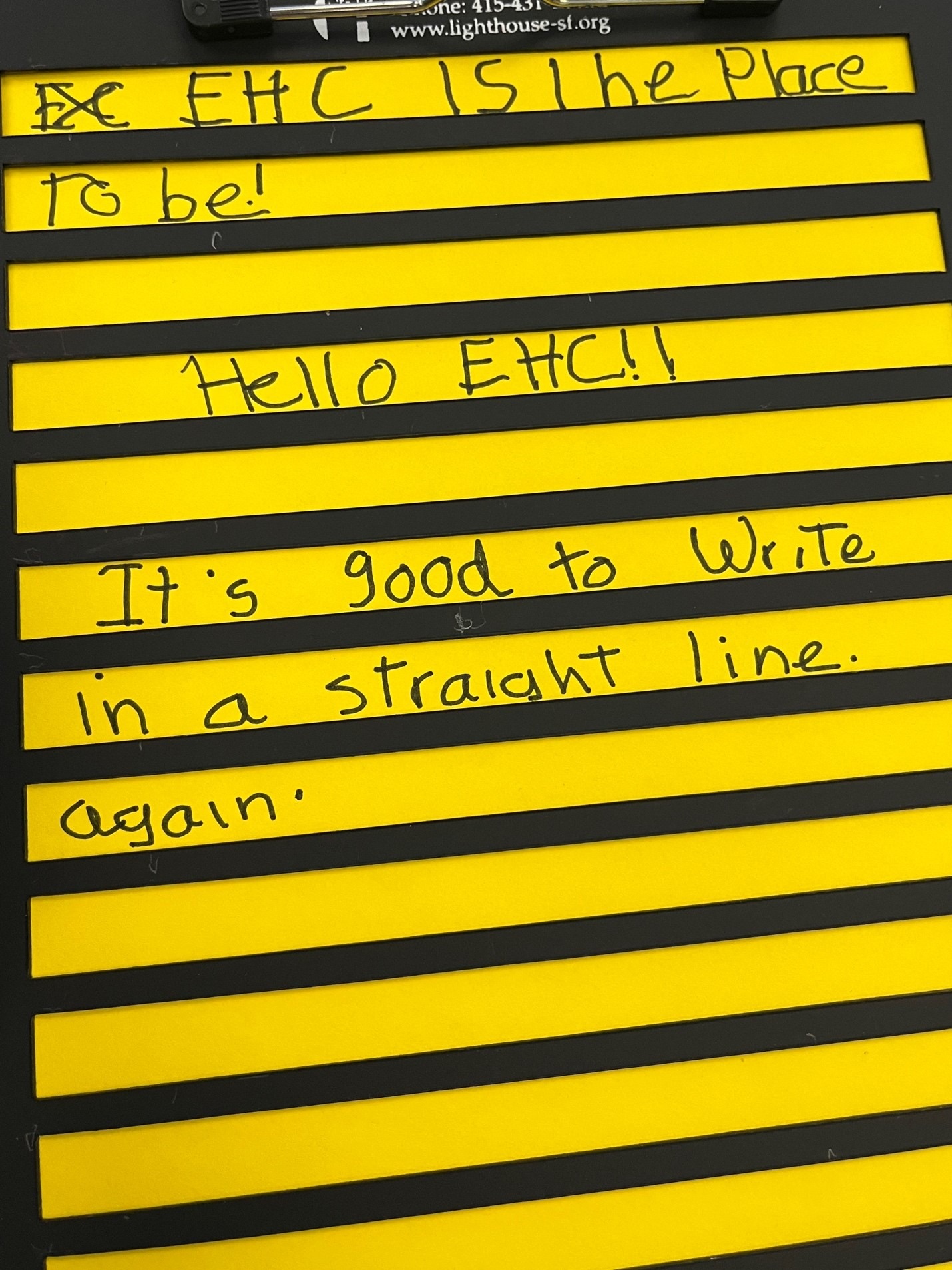A letter writing guide over a yellow piece of paper with the words “It’s good to write in a straight line again” in the middle of the photo.