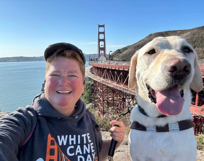 White Cane Day 2024 3 LightHouse CEO Sharon Giovinazzo and guide dog Pilot take a selfie with the bridge in the background.