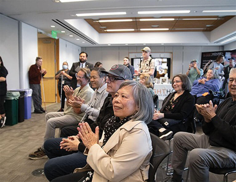 A room full of seated and standing attendees applaud at LightHouse Day 2023.