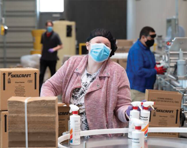 A LightHouse Eco employee wearing safety gear packs Skilcraft pump spray packs into boxes for shipping.