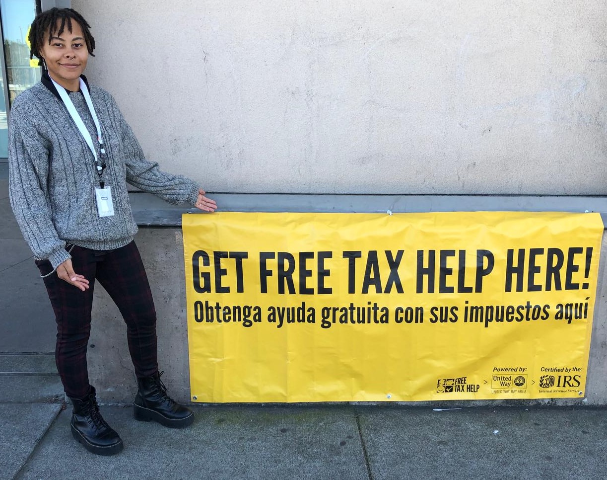 A person holding a sign that reads get your free tax help here!